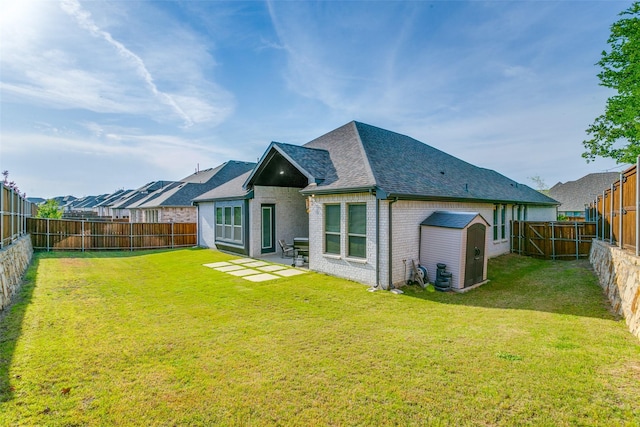 rear view of property with roof with shingles, brick siding, a shed, a fenced backyard, and a lawn