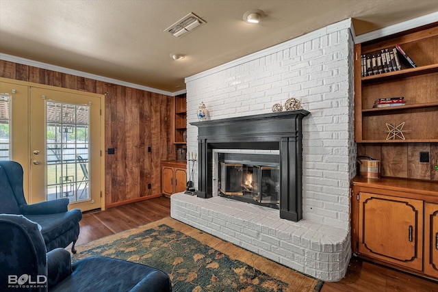 living area featuring a brick fireplace, wood walls, ornamental molding, visible vents, and dark wood-style floors