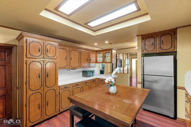 kitchen with brown cabinetry, freestanding refrigerator, crown molding, dark wood-style floors, and light countertops
