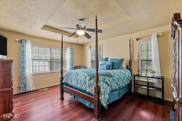 bedroom with baseboards, a tray ceiling, a textured ceiling, and wood finished floors