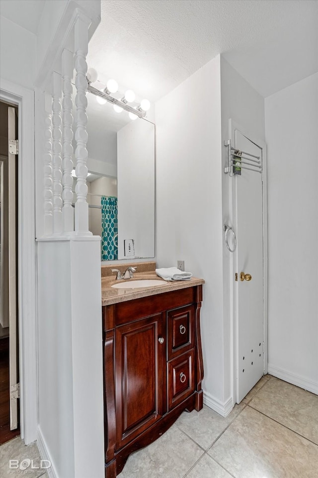 bathroom with a textured ceiling, tile patterned floors, baseboards, and vanity