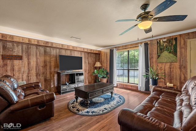 living room with wooden walls, a ceiling fan, ornamental molding, and wood finished floors