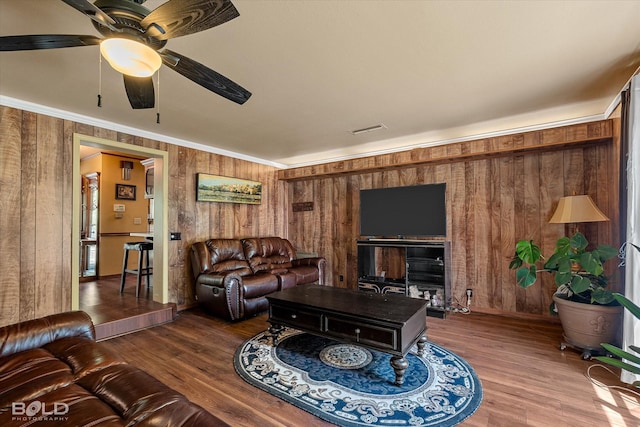 living area featuring visible vents, crown molding, wood finished floors, wooden walls, and a ceiling fan