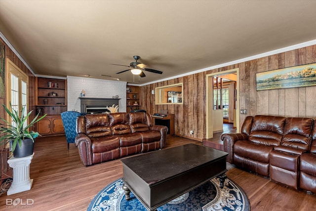 living area with crown molding, ceiling fan, light wood finished floors, a fireplace, and wood walls