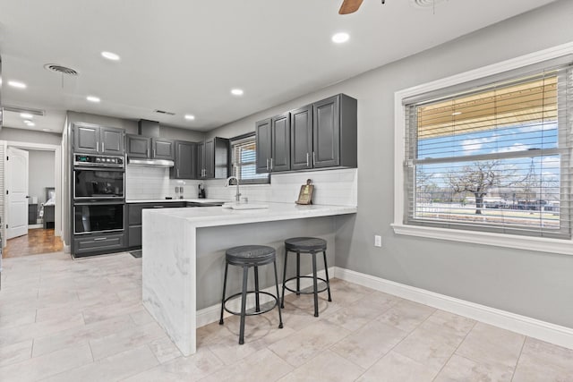 kitchen with dobule oven black, decorative backsplash, a peninsula, a kitchen breakfast bar, and light countertops