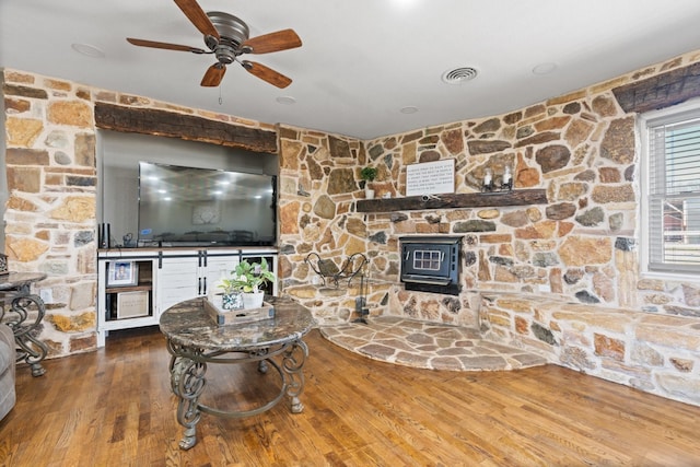 living area with a ceiling fan, wood finished floors, and a wood stove