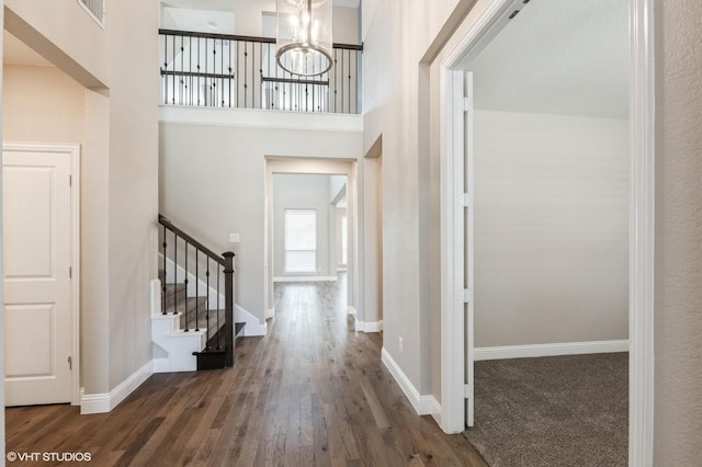 entryway with wood finished floors, baseboards, a chandelier, a high ceiling, and stairs
