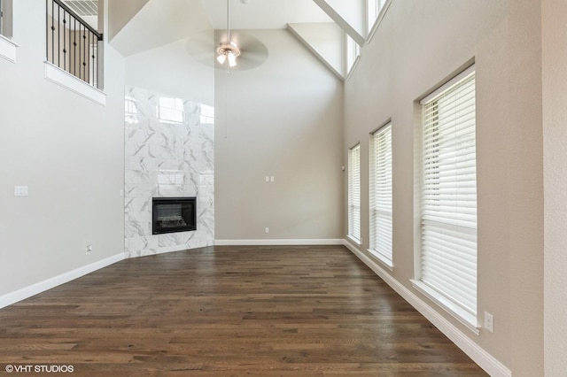 unfurnished living room with a towering ceiling, a fireplace, baseboards, dark wood-style floors, and a ceiling fan