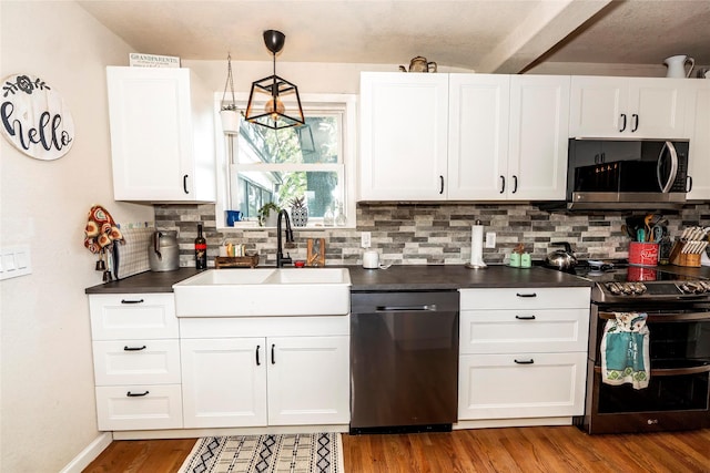 kitchen with dark countertops, white cabinets, a sink, backsplash, and stainless steel appliances