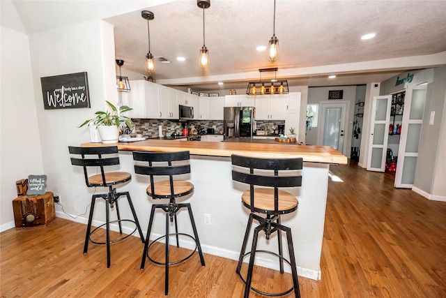 kitchen with a breakfast bar area, stainless steel appliances, a peninsula, tasteful backsplash, and butcher block counters