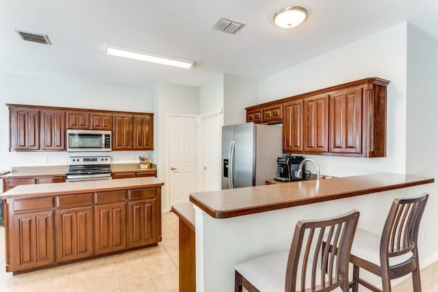 kitchen with stainless steel appliances, visible vents, a kitchen breakfast bar, and a peninsula