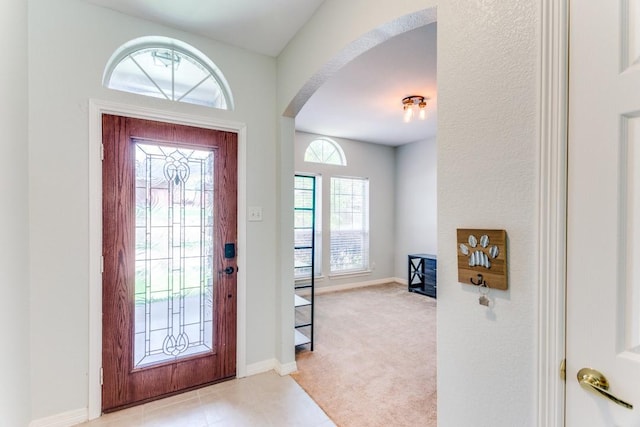 entrance foyer with arched walkways, baseboards, and light colored carpet
