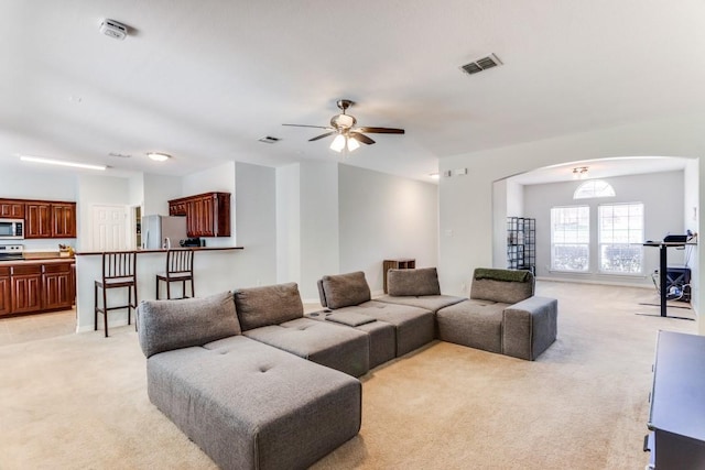 living area with visible vents, arched walkways, ceiling fan, and light carpet
