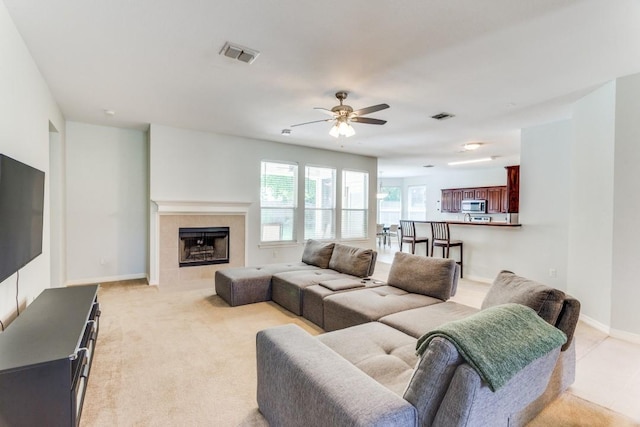 living room with light colored carpet, ceiling fan, visible vents, and a tile fireplace