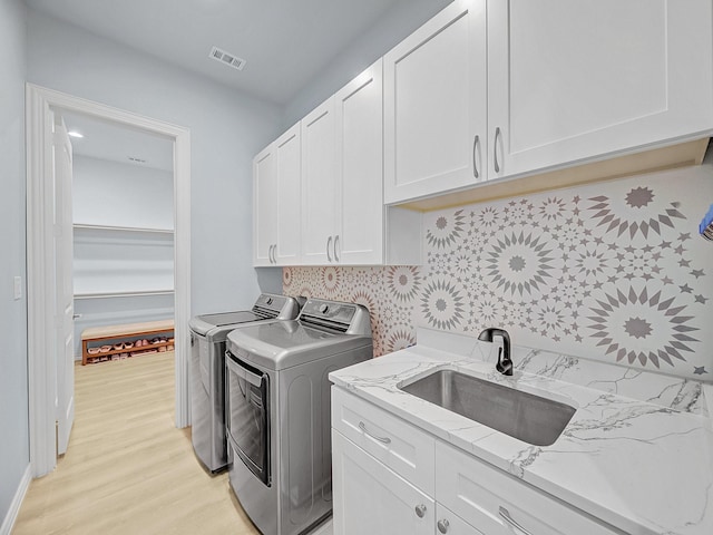 washroom featuring visible vents, washing machine and clothes dryer, cabinet space, a sink, and light wood finished floors