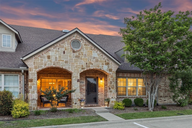 french country inspired facade with a shingled roof, brick siding, and stone siding