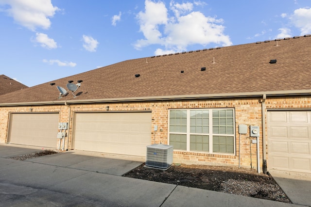 view of side of home featuring brick siding, cooling unit, and roof with shingles
