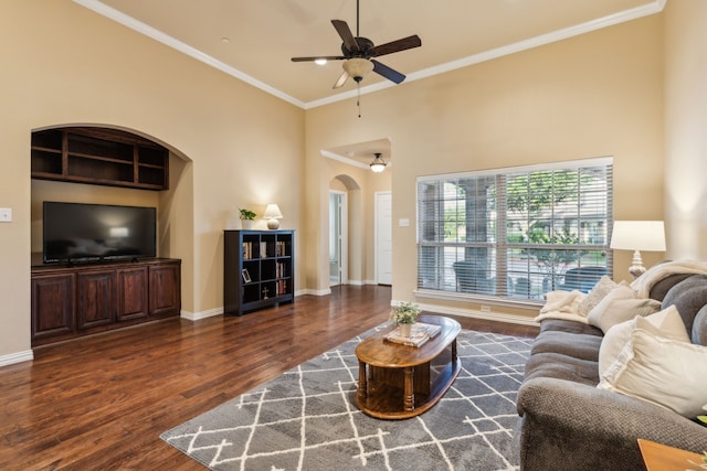 living room featuring crown molding, ceiling fan, arched walkways, baseboards, and wood finished floors