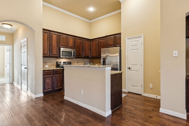 kitchen featuring crown molding, dark brown cabinetry, arched walkways, dark wood finished floors, and appliances with stainless steel finishes