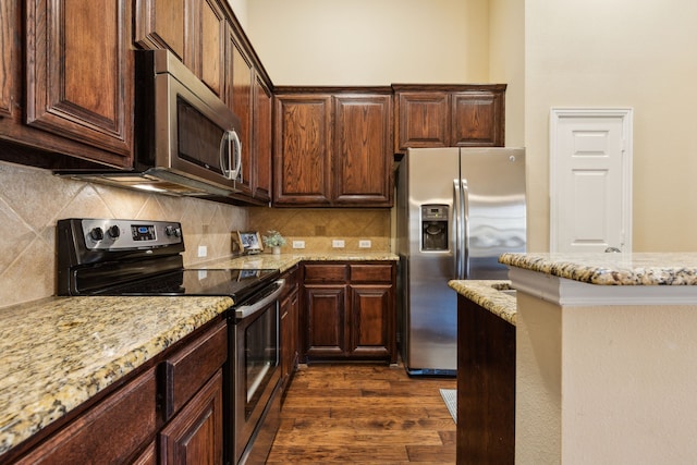 kitchen featuring dark wood-style flooring, dark brown cabinets, appliances with stainless steel finishes, light stone counters, and backsplash