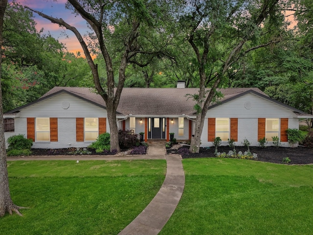 ranch-style home with a yard, brick siding, and a chimney