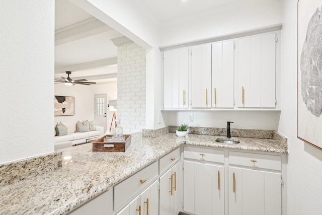 kitchen with a sink, light stone countertops, and white cabinetry