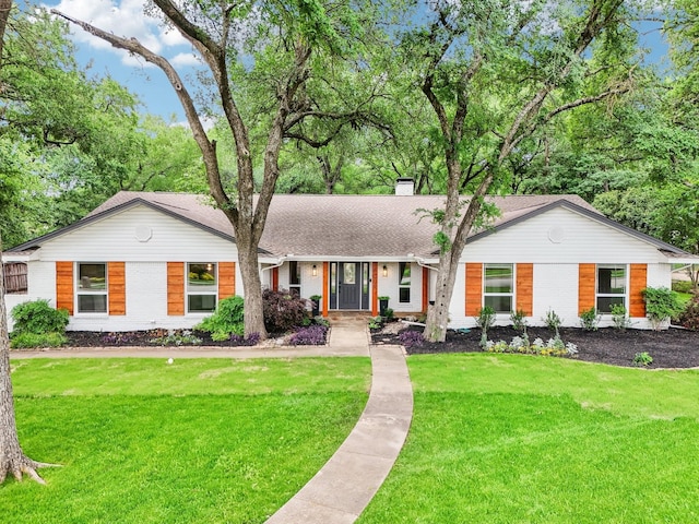 ranch-style home featuring brick siding, roof with shingles, a front yard, and a chimney