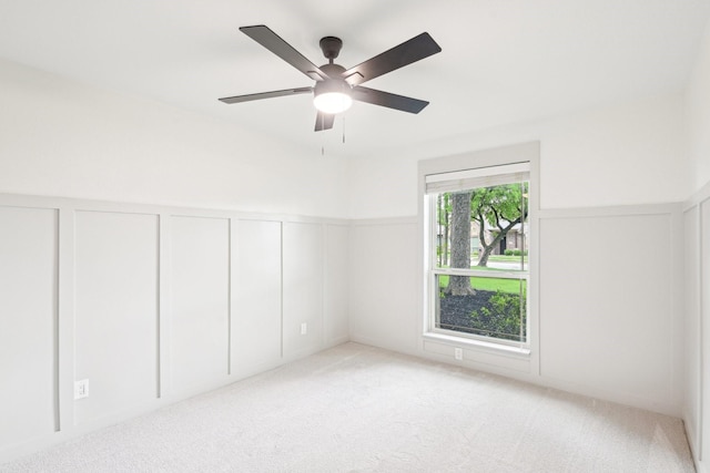 spare room with wainscoting, a decorative wall, and light colored carpet
