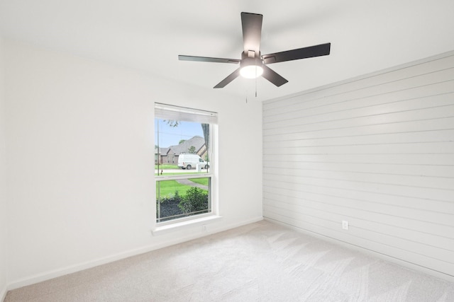 carpeted empty room with wooden walls, ceiling fan, and baseboards