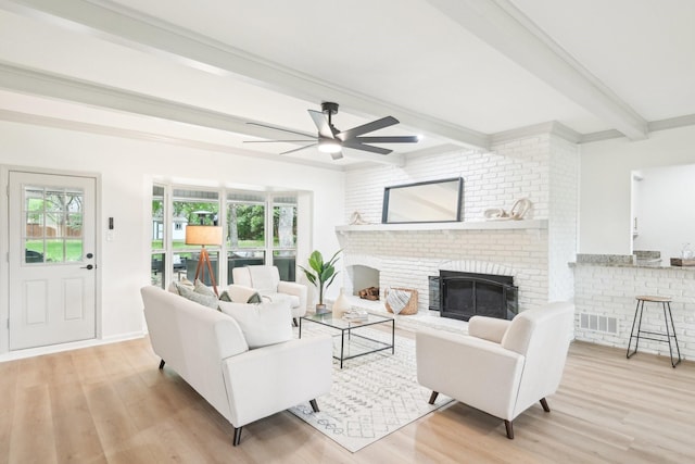 living area featuring ceiling fan, beam ceiling, a brick fireplace, and wood finished floors