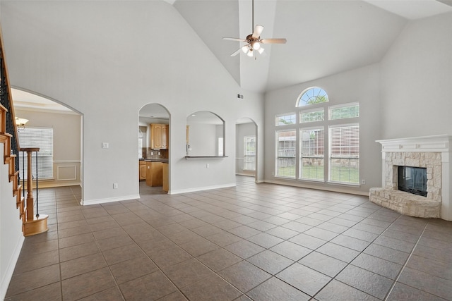 unfurnished living room with ceiling fan, high vaulted ceiling, a stone fireplace, dark tile patterned floors, and visible vents