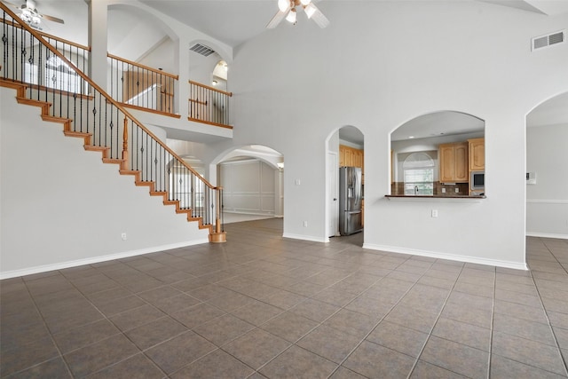 unfurnished living room featuring dark tile patterned flooring, ceiling fan, and a towering ceiling