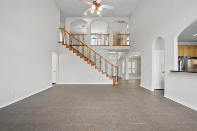 unfurnished living room with tile patterned flooring, ceiling fan, visible vents, and a towering ceiling