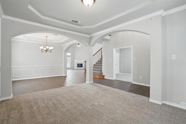 carpeted spare room featuring tile patterned flooring, a fireplace with raised hearth, a raised ceiling, and visible vents