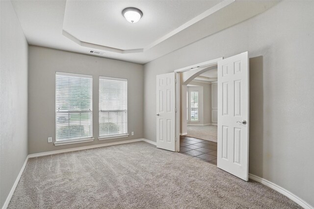 carpeted spare room featuring visible vents, arched walkways, tile patterned flooring, baseboards, and a tray ceiling