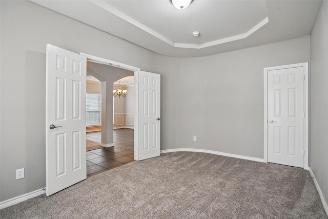 unfurnished bedroom with a raised ceiling, arched walkways, tile patterned floors, carpet, and baseboards