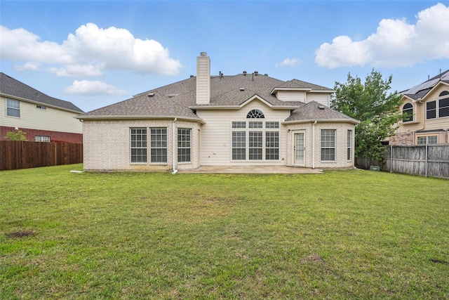 back of house with brick siding, a fenced backyard, a chimney, a patio area, and a lawn