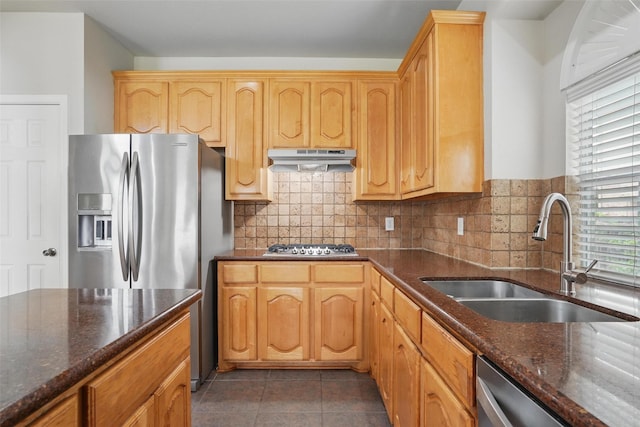 kitchen with a sink, dark stone counters, stainless steel appliances, and under cabinet range hood