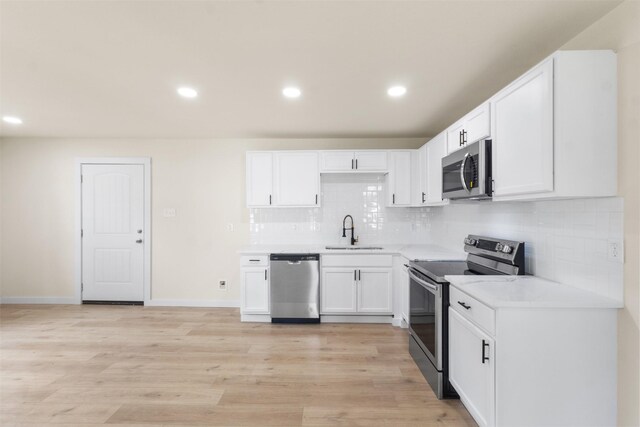 kitchen featuring appliances with stainless steel finishes, a sink, light countertops, white cabinetry, and recessed lighting