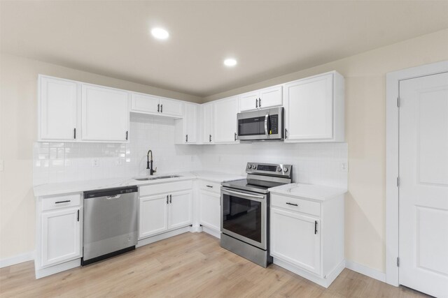 kitchen with stainless steel appliances, a sink, white cabinetry, light wood finished floors, and light countertops