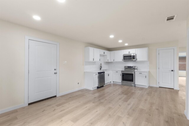 kitchen featuring appliances with stainless steel finishes, a sink, light wood-type flooring, white cabinetry, and light countertops