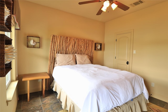 bedroom with stone finish floor, a ceiling fan, visible vents, a fireplace, and baseboards