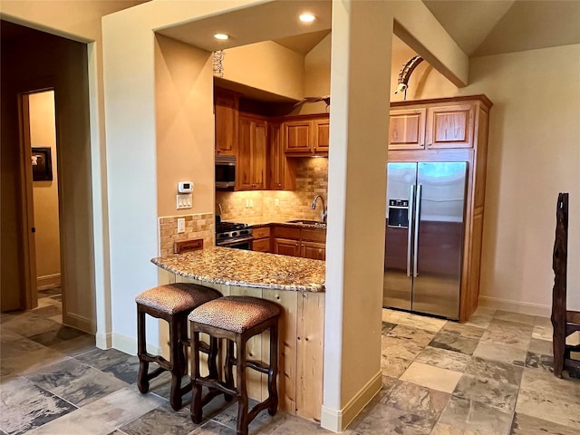 kitchen with backsplash, appliances with stainless steel finishes, light stone countertops, a sink, and stone tile flooring