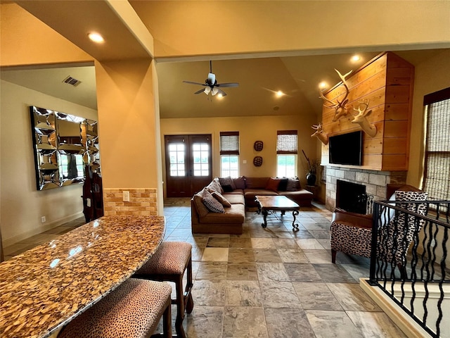 living area featuring visible vents, stone tile flooring, ceiling fan, a tiled fireplace, and vaulted ceiling