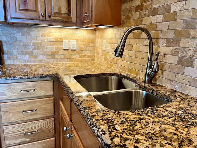 kitchen featuring a sink, dark stone counters, backsplash, and brown cabinets
