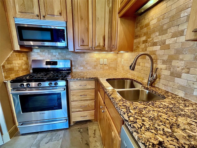 kitchen featuring brown cabinetry, tasteful backsplash, light stone counters, a sink, and stainless steel appliances