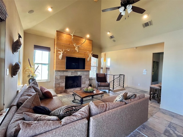 living area featuring baseboards, ceiling fan, a stone fireplace, and visible vents