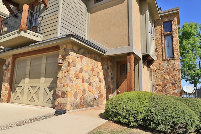 view of home's exterior with a garage, stucco siding, a balcony, and stone siding