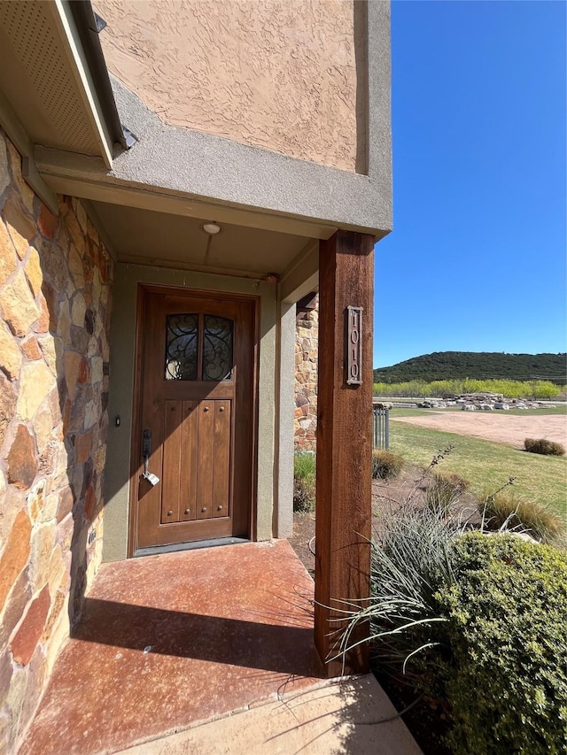 property entrance with a mountain view, stucco siding, and stone siding