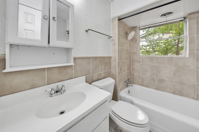 bathroom with vanity, visible vents, toilet, tile walls, and shower / bathing tub combination